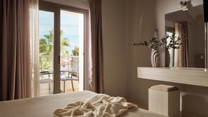 A hotel room with a bed, a large window with curtains, a view of the outdoors, a small table with chairs, and a mirror with a vase of flowers. - Atlantis Hotel (Zakynthos)