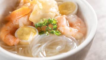 A bowl of noodle soup with shrimp, egg, and vegetables.