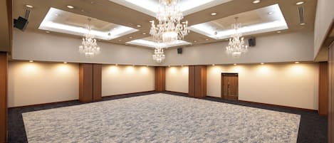 Un'ampia sala conferenze ben illuminata, con tappeto a motivi, pannelli in legno e un lampadario centrale.