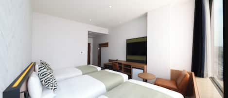 A modern hotel room with two beds, a desk, a television, and a view of the city.