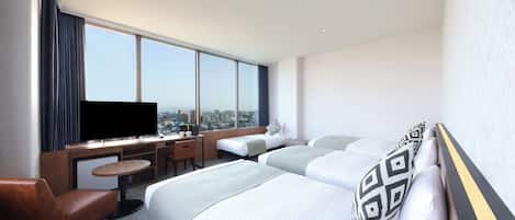 Habitación de hotel con un ventanal grande, un escritorio con televisor de pantalla plana, dos camas, un sofá y una mesita.
