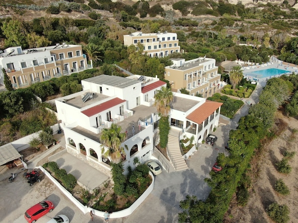 An aerial view of a residential area with modern buildings, a swimming pool, and surrounding greenery. - Hermes Hotel (Kos)