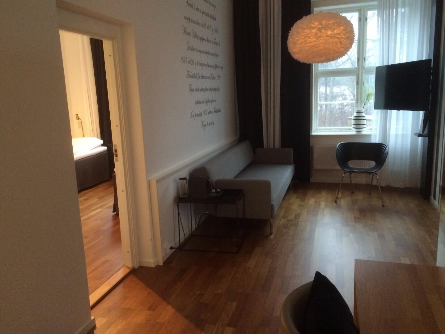 A modern living room with a sofa, a small table, a chair, and a large window with curtains.