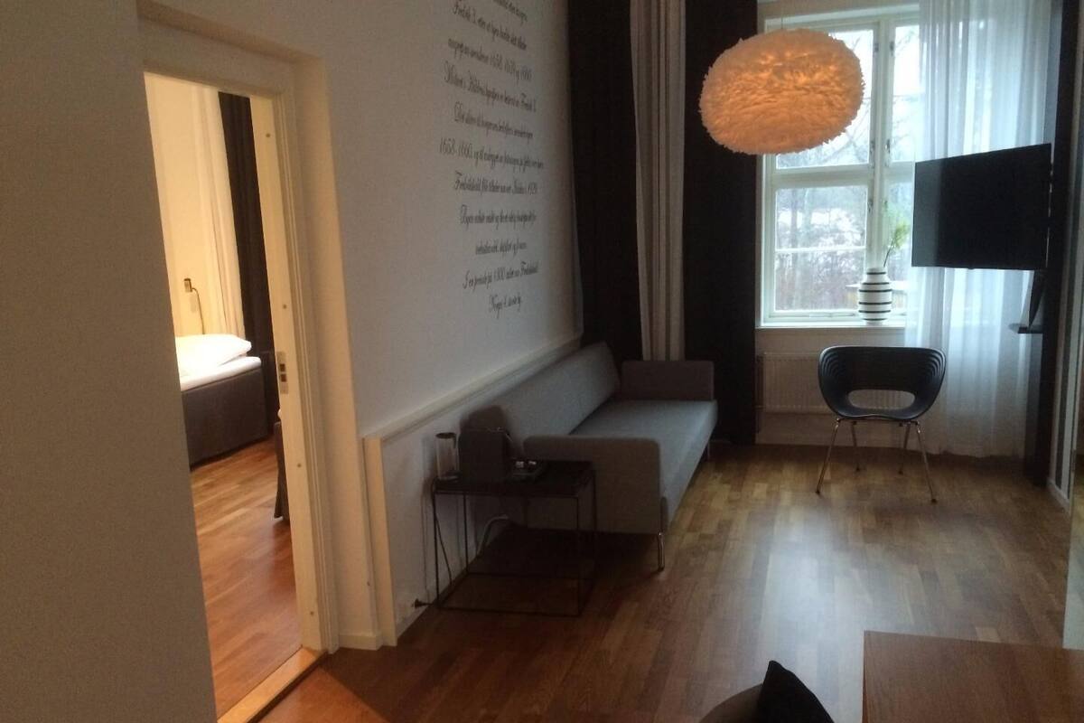 A modern living room with a sofa, a small table, a chair, and a large window with curtains.