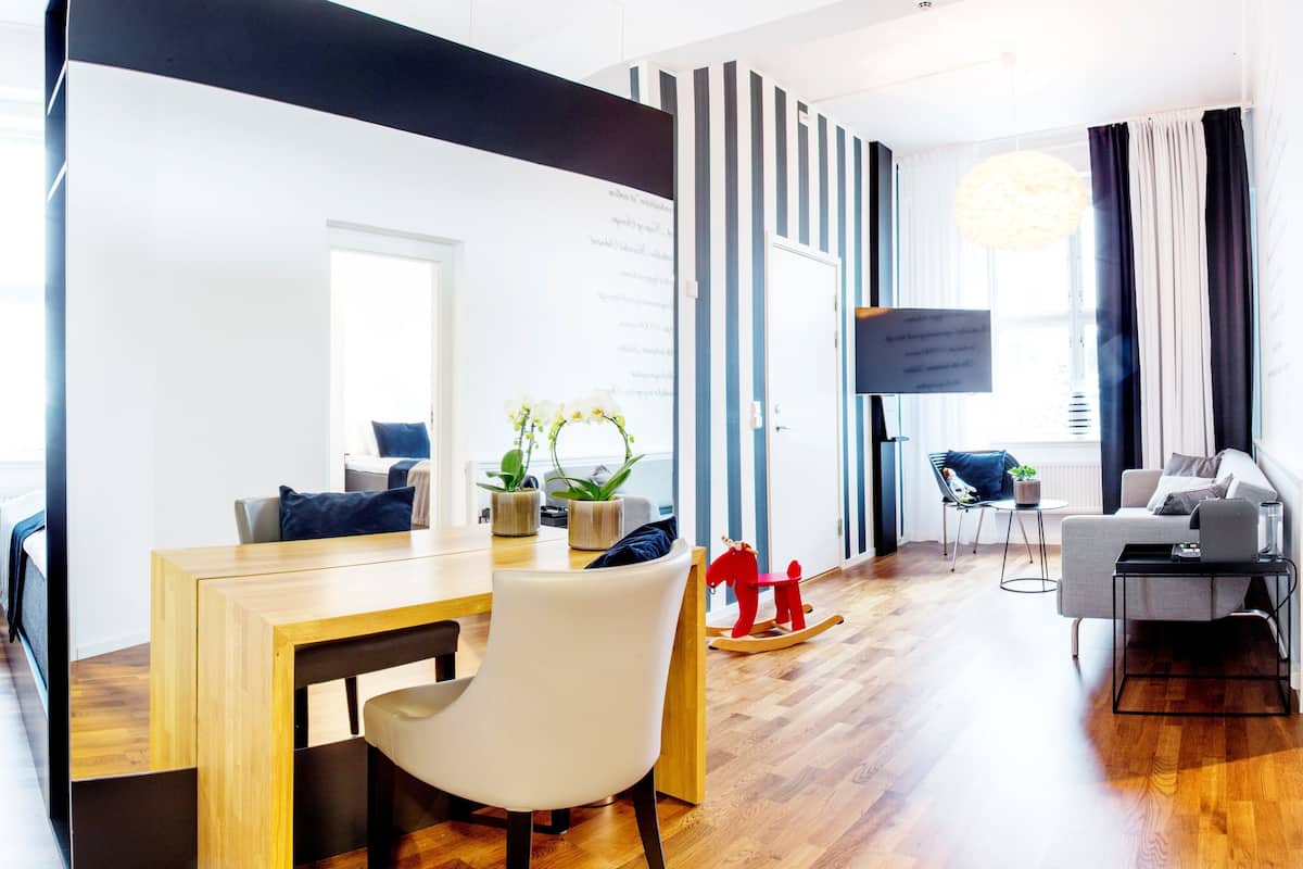 A modern living room with a wooden dining table, a white chair, a red rocking horse, and a grey sofa.