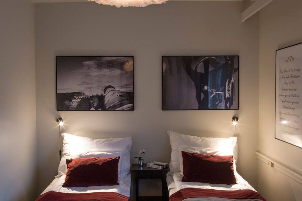 A bedroom with two beds, a chandelier, and two framed pictures on the wall.