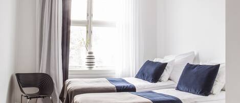 Un dormitorio con dos camas, una silla y una ventana con cortinas.