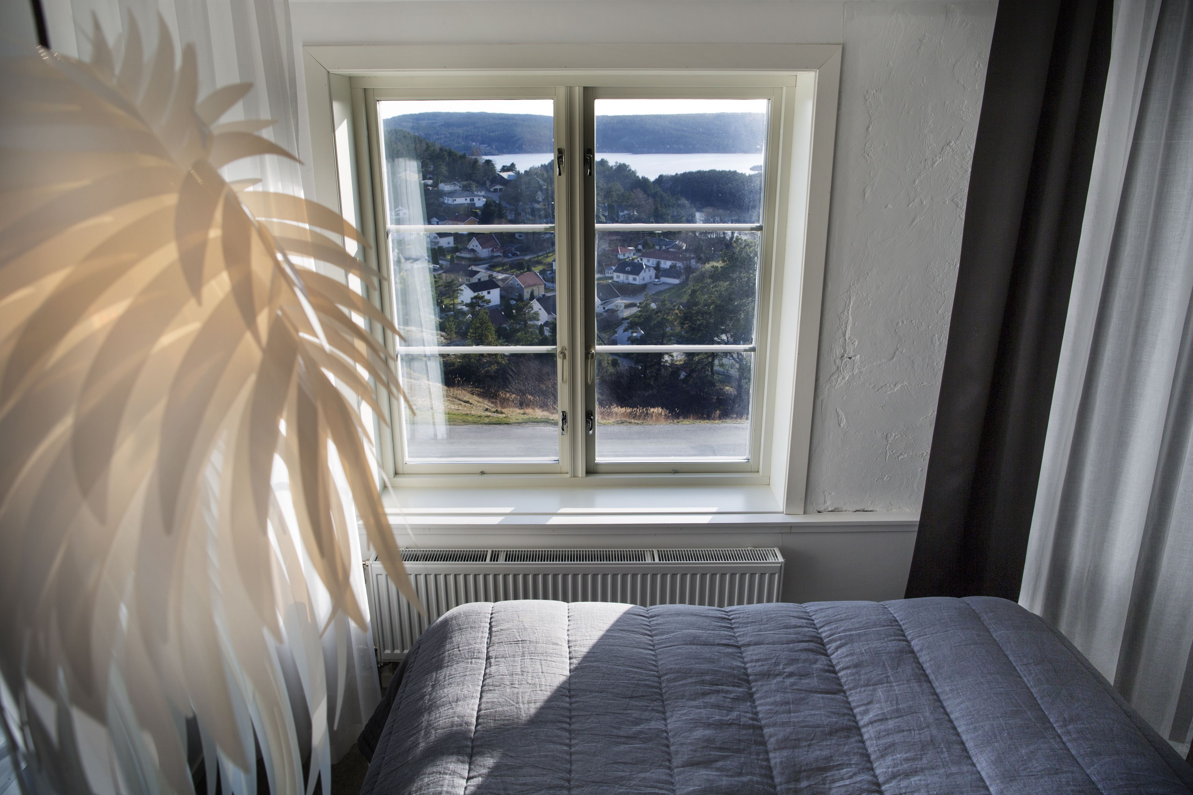 Een slaapkamer met een bed, een radiator en een raam met uitzicht op een stad en heuvels.