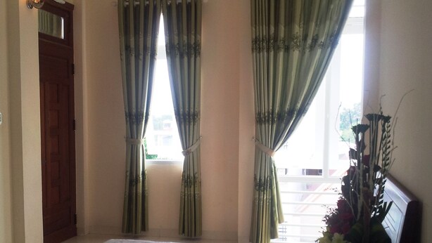 A hotel room with a bed, a desk with a vase of flowers, and a window with curtains. - Seaside Hotel 2 (Nha Trang)