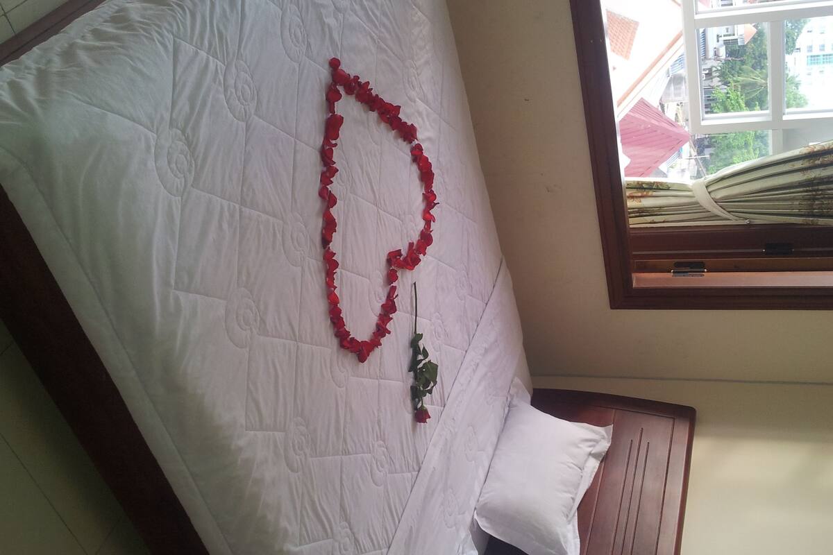 A bed with a white quilt and a red rose arrangement.