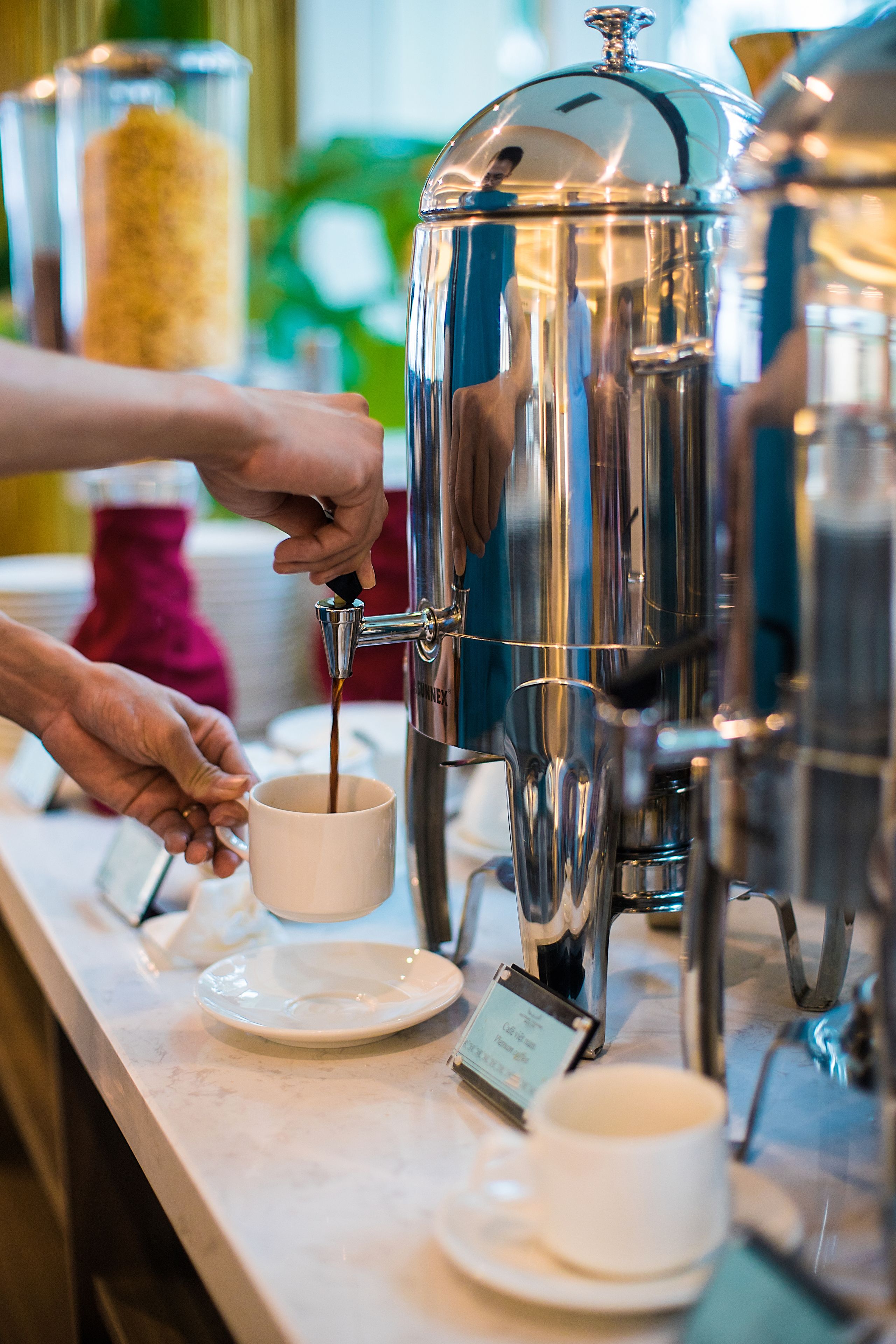 A coffee station with a coffee dispenser and cups on a marble countertop.