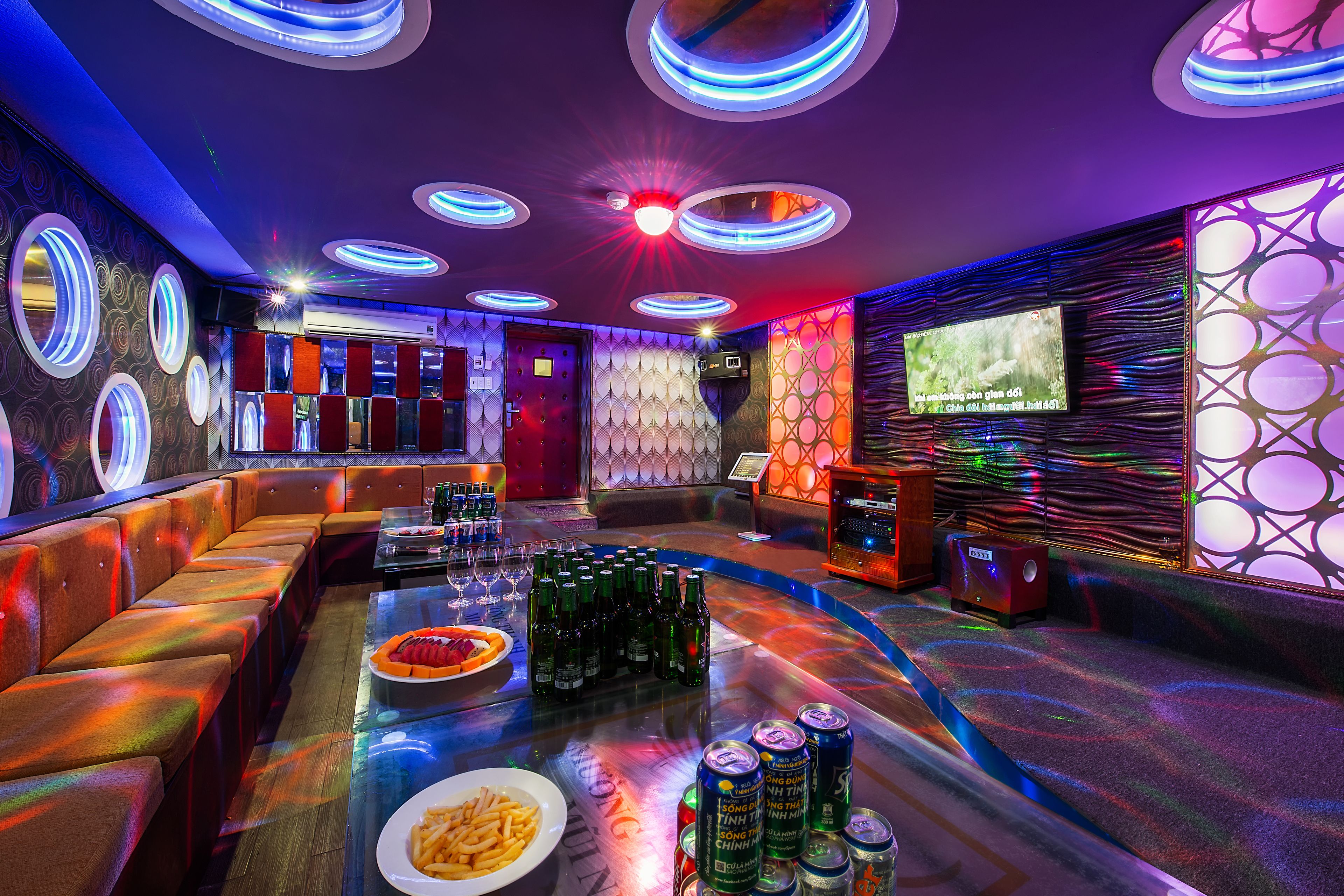 Zona de bar con luces de neón, asientos y una pantalla de televisión.