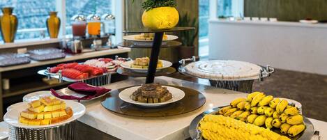 A buffet with various food items, including a banana display and a cake on a tiered stand.