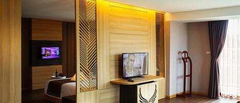 A modern hotel room with a wooden floor, a bed, a TV on a wooden stand, and a large window with curtains.