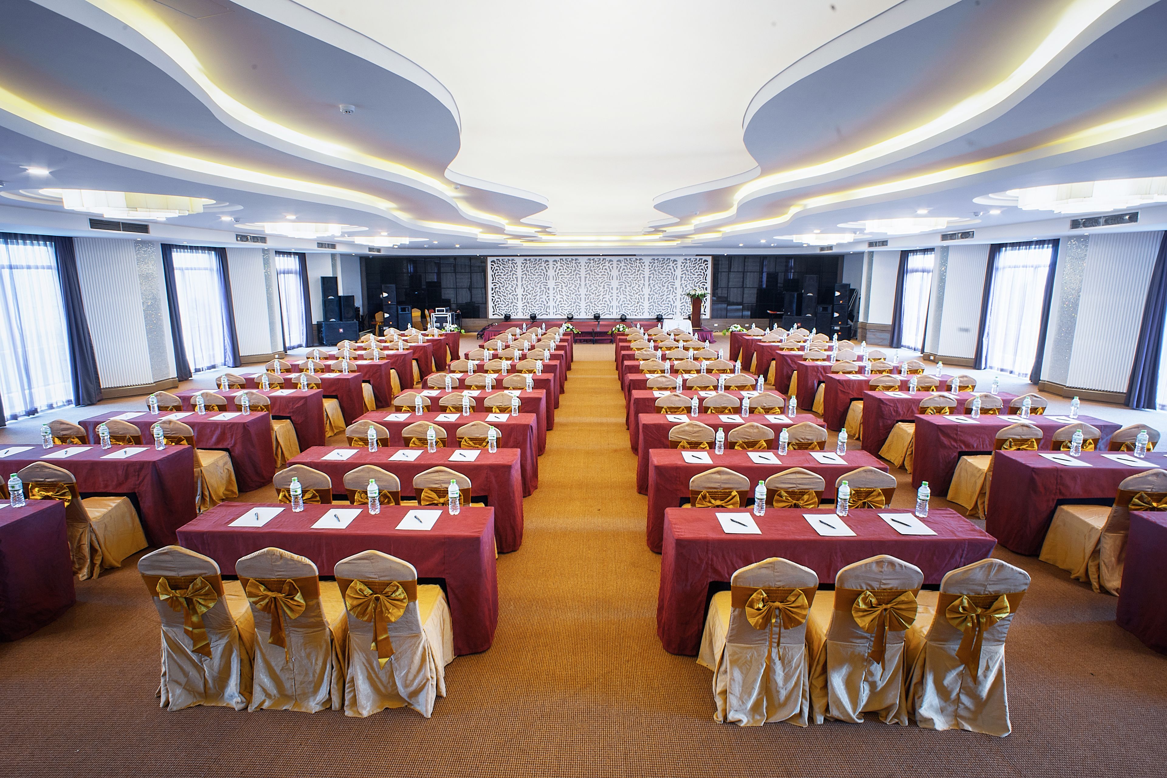 A conference room with rows of tables and chairs, a stage at the front, and a patterned wall backdrop.