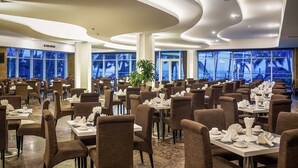 Un comedor espacioso con varias mesas y sillas, ventanas amplias con vistas y un diseño moderno de techo.