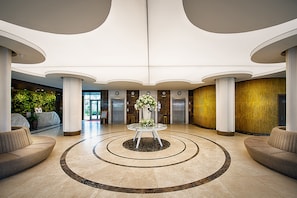 Eine großzügige Lobby mit einer zentralen, runden Sitzecke, großen Säulen und einem modernen Deckenbau.