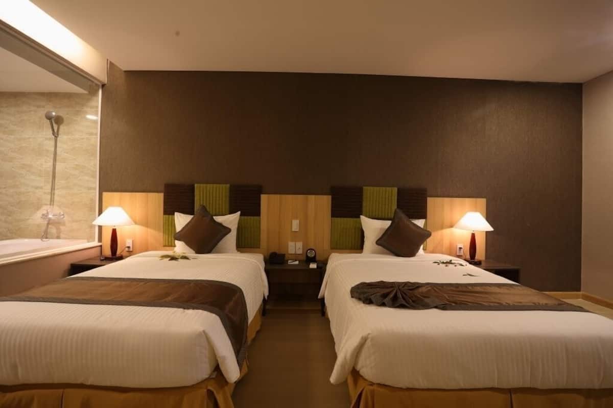 A hotel room with two beds, a bathroom, and a nightstand with a lamp.