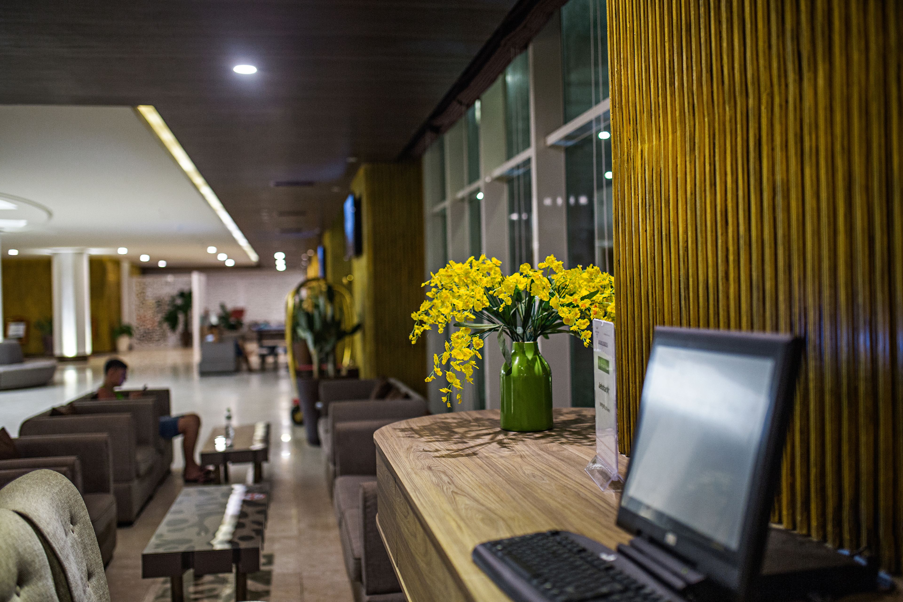 A modern hotel lobby with seating areas, a reception desk, and a laptop on the counter.