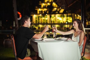 Una pareja cenando al aire libre de noche, con una mesa para dos, una vela y una botella de vino.