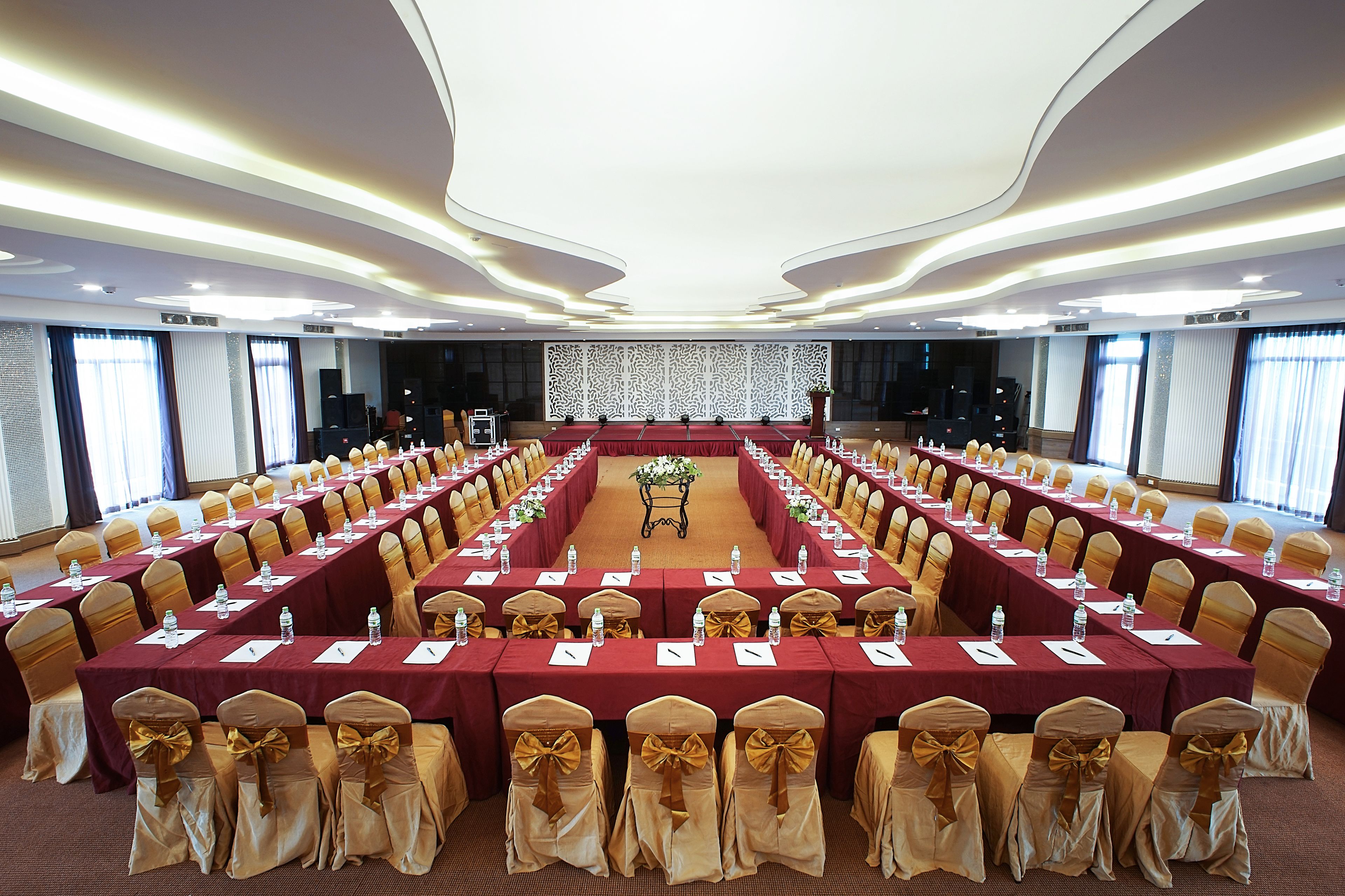 Un salón de conferencias con largas mesas, sillas y un escenario.