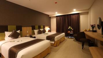 A hotel room with two beds, a desk, a chair, a small table with flowers, and a mirror on the wall.