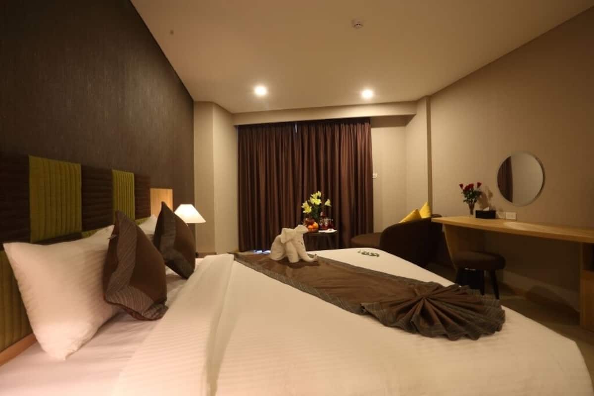 A hotel room with a bed, a desk, a chair, a mirror, and a window with curtains.