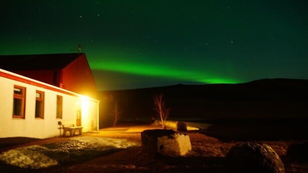 A building with a red roof and a lit interior, set against a backdrop of the northern lights.