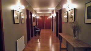 A hallway with wooden flooring, framed pictures on the walls, and a bench with a vase of dried plants.