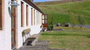 A building with a red roof, a wooden bench outside, and a grassy hill in the background.