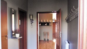 A hallway with a tiled floor, a ceiling fan, a door leading to another room, and a wall-mounted light fixture.