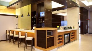 A modern bar area with a counter, bar stools, a television, and shelves with bottles. - Hampton Inn by Hilton Silao-Aeropuerto Bajio (Silao)