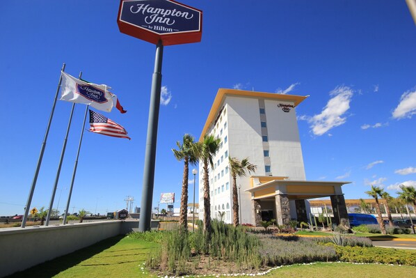 A Hampton Inn by Hilton hotel with a clear blue sky, American flags, and a well-maintained garden. - Hampton Inn by Hilton Silao-Aeropuerto Bajio (Silao)