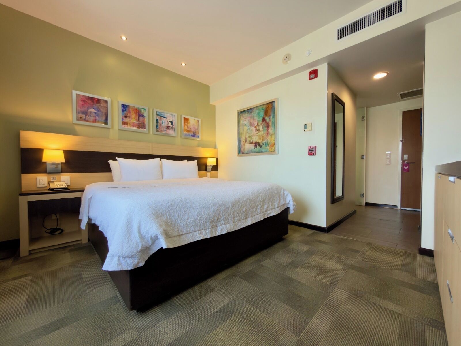 Een hotelkamer met een bed, bedlampen, een bureau en een schilderij aan de muur.