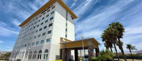 A multi-story hotel with a flat facade, a covered entrance, and a parking lot with yellow curbs.