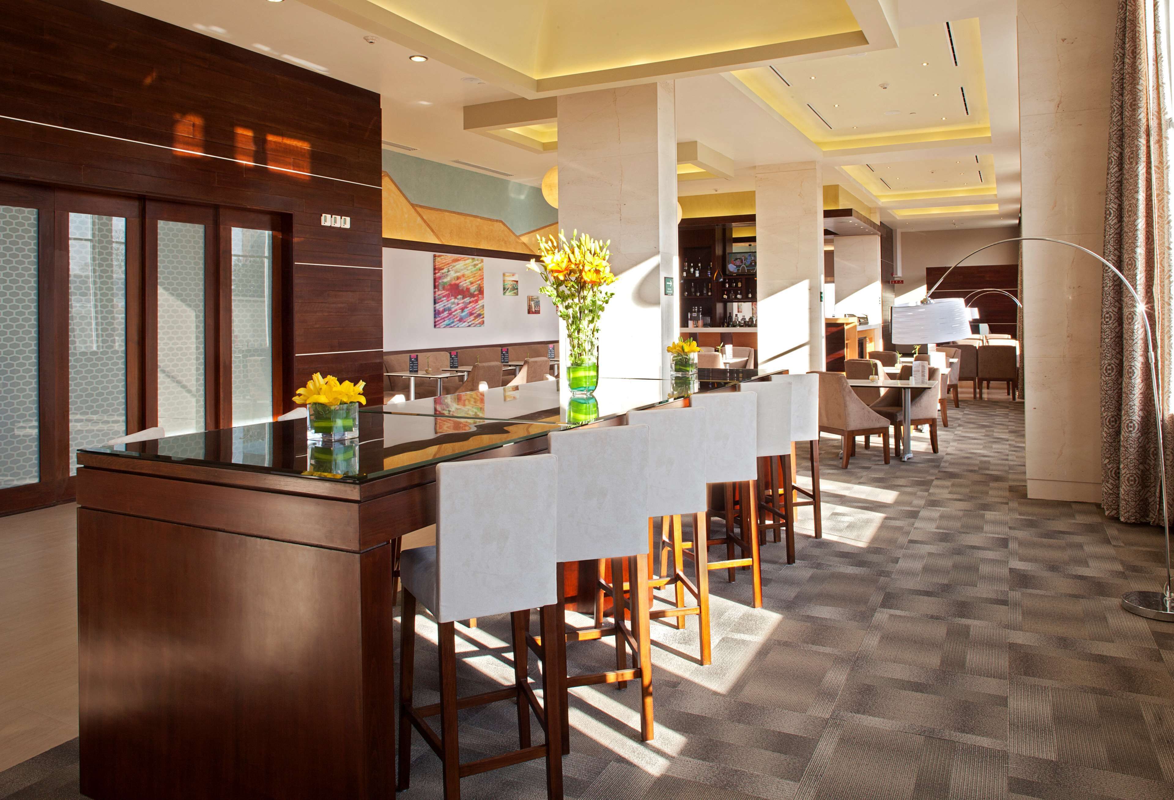 A modern hotel lobby with a reception desk, bar area, and seating.