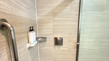 A modern shower with a glass door, a handrail, and a shelf with toiletries.