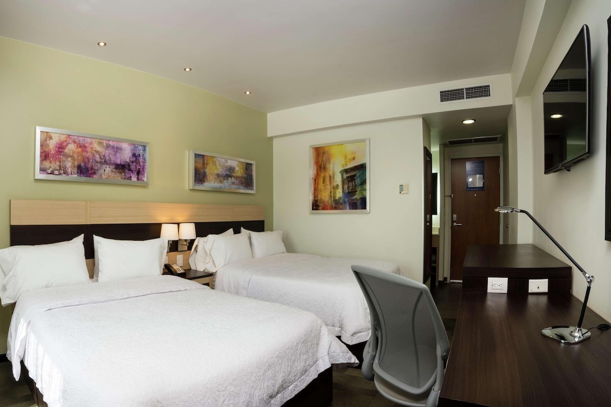 Habitaci ón de hotel con dos camas, un escritorio, una silla y obras de arte en las paredes.