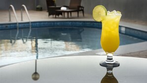 A glass of yellow drink with a lime slice on a table near a swimming pool. - Hampton Inn by Hilton Silao-Aeropuerto Bajio (Silao)