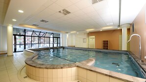 An indoor swimming pool with a tiled floor and a curved edge, a glass door leading outside, and a shower area with a white wall and a door. - Noemys Castor & Pollux (Risoul)