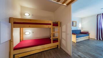 A bunk bed with a red mattress, a wooden floor, a small table with a cushion, and a wall-mounted light fixture.