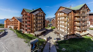 A modern ski resort with wooden buildings, outdoor seating, and mountain views. - Noemys Castor & Pollux (Risoul)