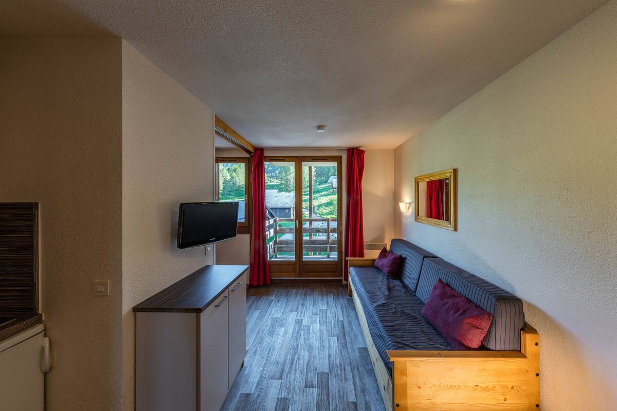 A room with a sofa, a television, a wooden bench, and a sliding glass door leading to an outdoor area.