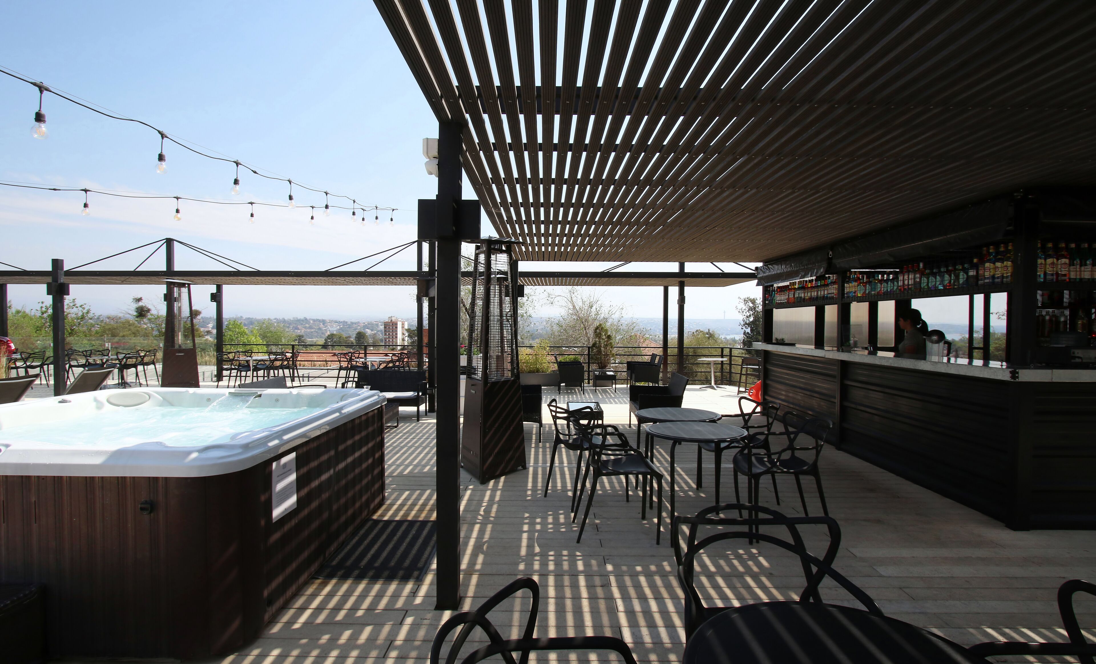 An outdoor patio with a hot tub, seating area, and bar with a view of the city.