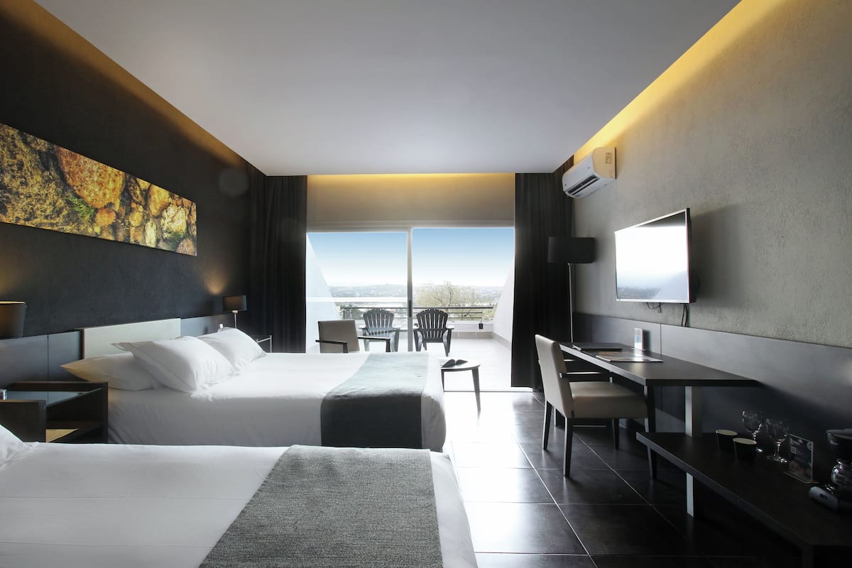 Une chambre d’hôtel moderne avec deux lits, un bureau, une télévision et un balcon offrant une vue sur la ville.