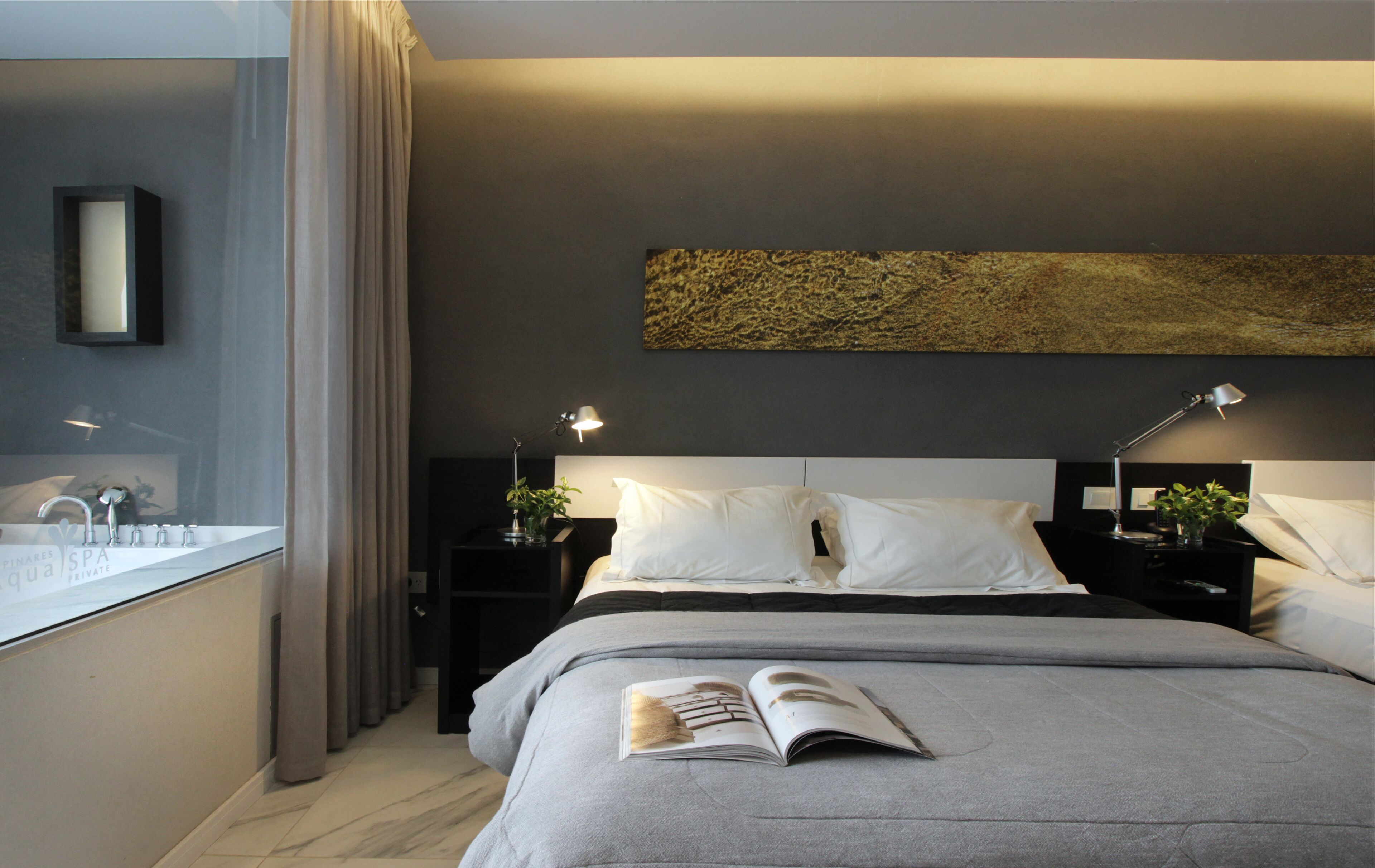 Un dormitorio moderno con una cama grande, lámparas de noche, una mesita de noche, un espejo y vistas al baño.