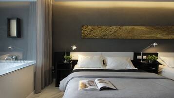 Un dormitorio moderno con una cama grande, lámparas de noche, una mesita de noche, un espejo y vistas al baño.