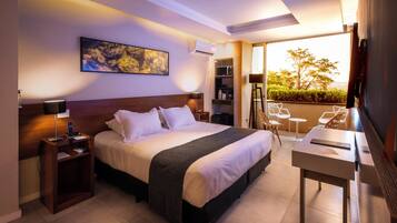 Habitación de hotel con cama, mesitas de noche, escritorio, silla, televisor y balcón con vistas.