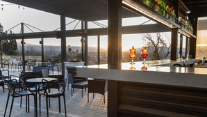 Een terras met een uitzicht op de bergen, tafels, stoelen en een divers aanbod aan flessen op de planken.