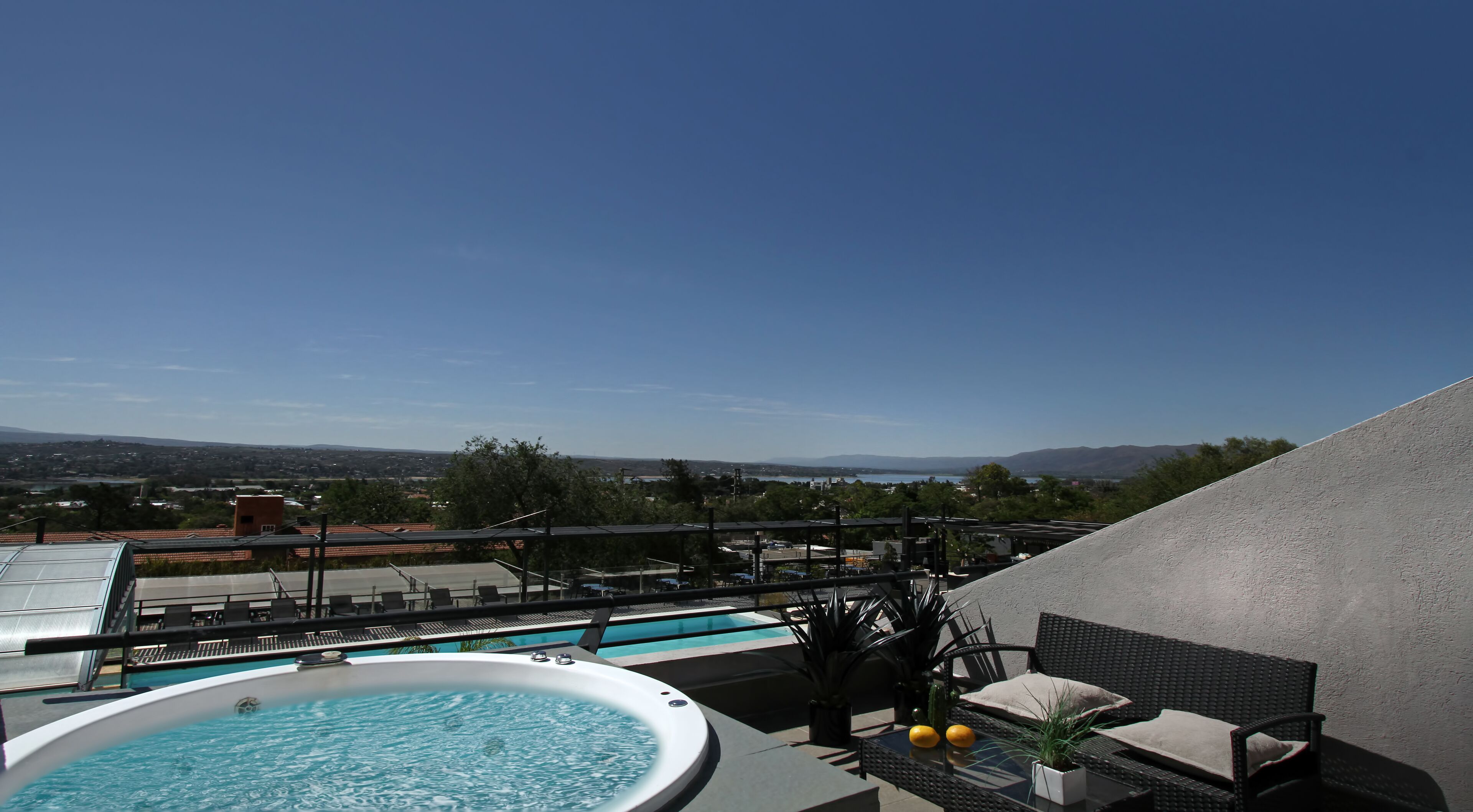 Un área de piscina en la azotea con vista a un paisaje urbano y montañas a lo lejos.